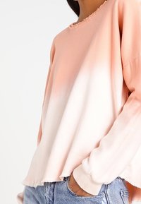 Lichtgewicht, dip-geverfde sweatshirt in koraal en wit. Voorzien van een rafelige halslijn en zoom, met omgeslagen mouwen. De stof heeft een zachte textuur.