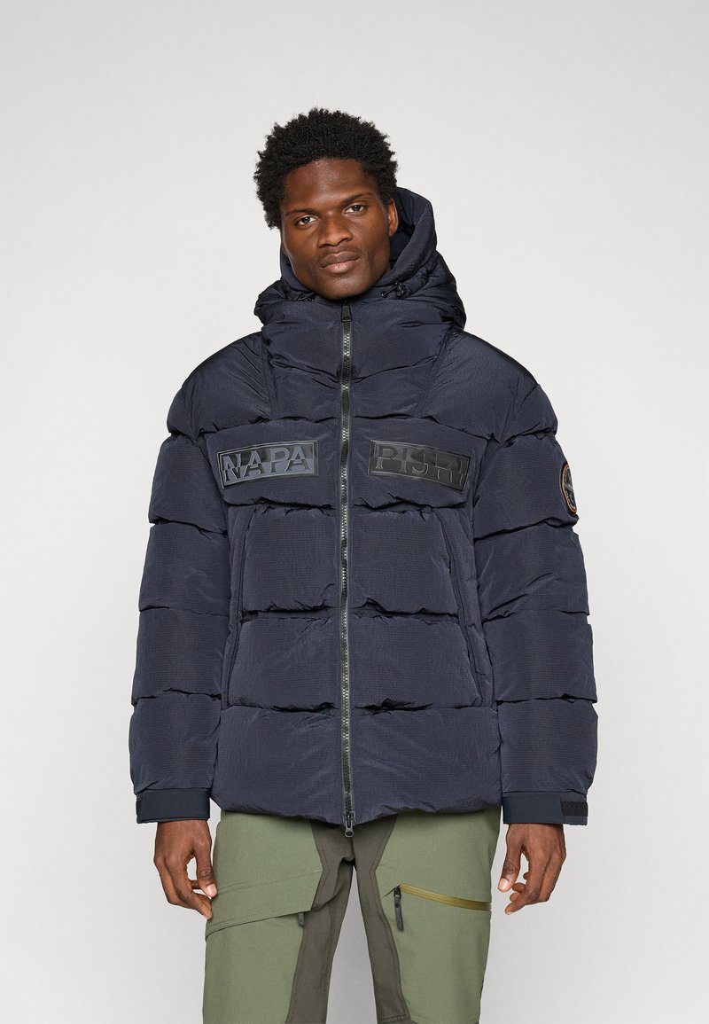 Doudoune marine avec capuche, dotée de sections surdimensionnées en quilts horizontaux, fermeture éclair à l'avant et grandes patches de logo noir sur la poitrine.