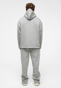 Lichtgrijze bijpassende hoodiesweater en broek, gemaakt van zachte stof. De hoodie heeft een comfortabele pasvorm, met een capuchon en ingezette schouders.