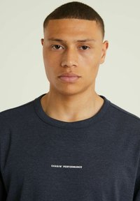 T-paita tummansinisestä pehmeästä kankaasta, jossa on pyöreä kaula-aukko ja valkoisella teksti painettuna rintaan: "CHASIN' PERFORMANCE."