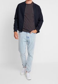 Chaqueta bomber azul marino con cremallera frontal, combinada con una camiseta azul marino a rayas, jeans de color azul claro y zapatillas blancas. Ajuste y diseño casual.