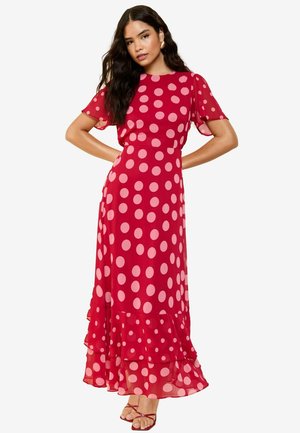 Red polka dot dress with short, sheer sleeves and a flounced hem. Fabric appears lightweight with a smooth texture. Adjustable straps on sandals.