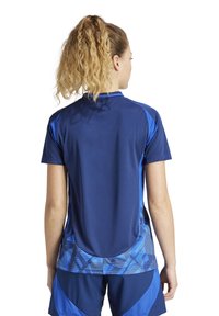 Maglietta sportiva blu con maniche corte, caratterizzata da un motivo geometrico testurizzato in diverse tonalità di blu sulla schiena e sulle spalle.