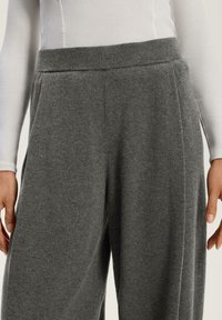 Grå ullblandade byxor med en mjuk textur, med ett brett midjeband, sidofickor och en avslappnad silhuett, framhämtade mot en ljus bakgrund.