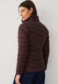 Giacca imbottita bordeaux con collo alto, motivo a chevron e polsini elasticizzati. Materiale morbido e leggero con branding discreto.