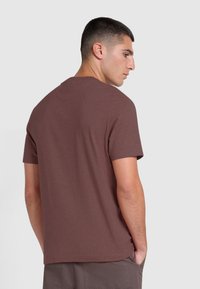 T-shirt in cotone marrone con maniche corte, scollatura tonda e una texture liscia, vista dalla parte posteriore. Design semplice senza loghi visibili.