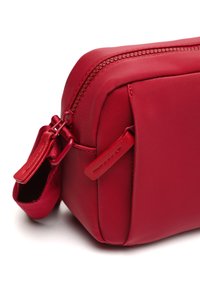 Borsa in nylon rosso di forma rettangolare, con chiusura a zip, superficie liscia e un piccolo anello in tessuto sul lato per un facile trasporto.