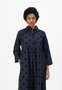 Vestito blu navy con colletto e maniche a tre quarti, caratterizzato da ricami floreali a intaglio e una vita arricciata per una vestibilità rilassata.