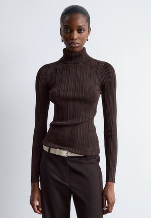 Brauner, gerippter Rollkragenpullover mit enganliegenden langen Ärmeln, aus einem strukturierten Strickstoff, kombiniert mit dunklen Hosen und einem hellen Gürtel.