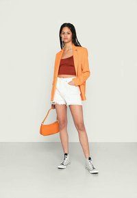 Blazer laranja, top cropped castanho, calções brancos com franjas e ténis pretos e brancos estampados. Inclui uma mala laranja. Texturas suaves.