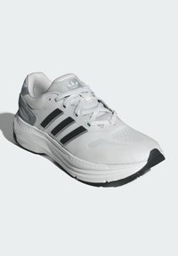 Zapatilla de running gris claro con acentos negros, parte superior de malla, superficie texturizada, tres franjas negras, suela acolchada y suela de goma.