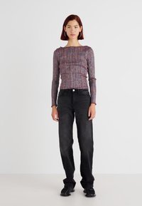 Ribbed long-sleeve top in multicolored knit, paired with straight-leg black jeans and dark sneakers, showcased on a model.