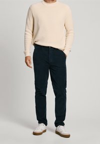 Cream ribbed sweater, navy corduroy pants, and white sneakers with tan soles. Outfit features a relaxed fit and textured fabric.