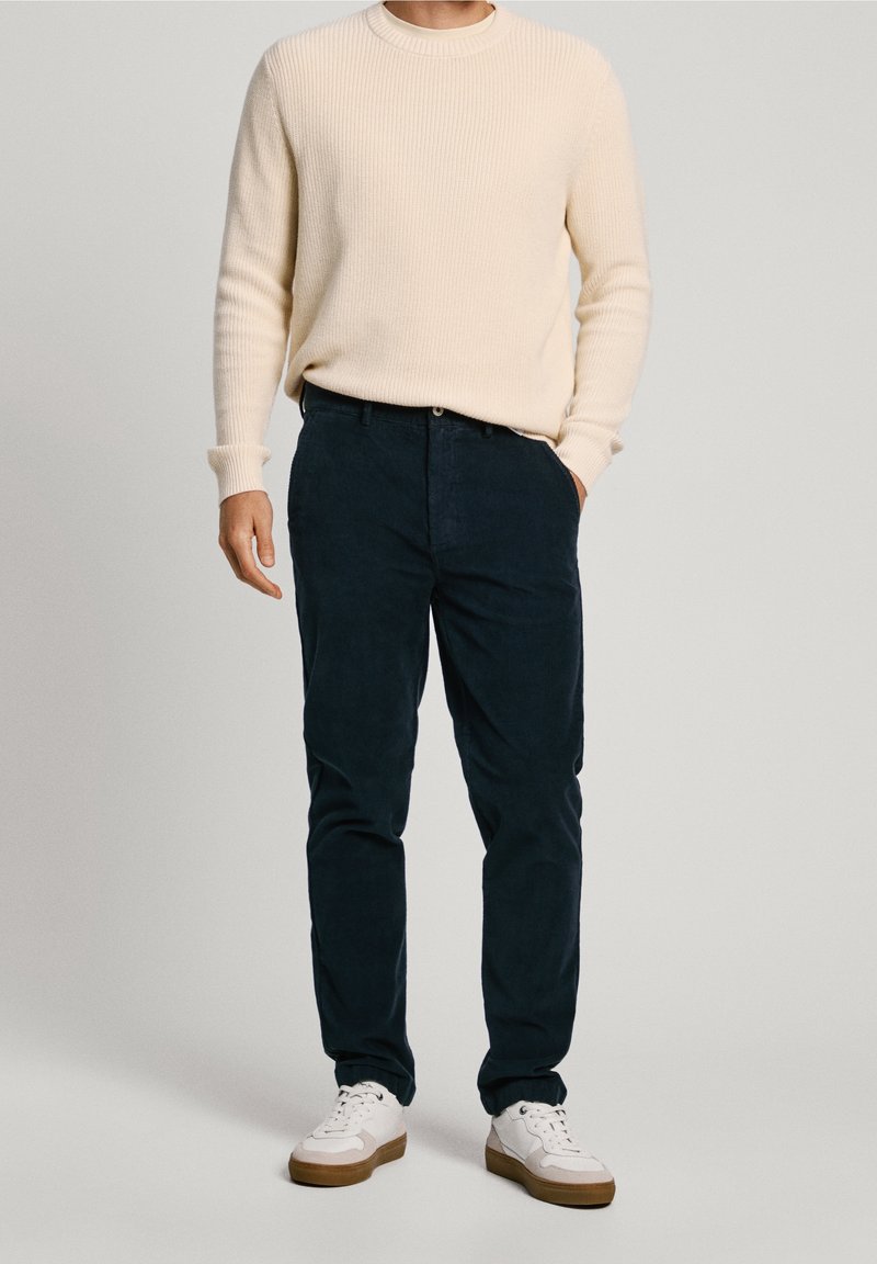 Cream ribbed sweater, navy corduroy pants, and white sneakers with tan soles. Outfit features a relaxed fit and textured fabric.