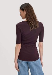 Bordeaux fitted top met korte mouwen, met een ronde halslijn en een gladde textuur, gecombineerd met lichtblauwe high-waisted jeans.