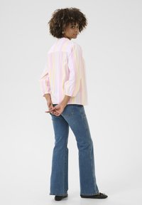 Blusa a righe pastello in rosa, giallo e bianco, con maniche a sbuffo, abbinata a jeans a campana blu e scarpe basse nere. Design semplice.