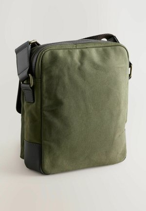 Olíva zöld vászon keresztpántos táska cipzárral, fekete bőrkiegészítőkkel, téglalap alakú, állítható pánttal. Sima textúra.