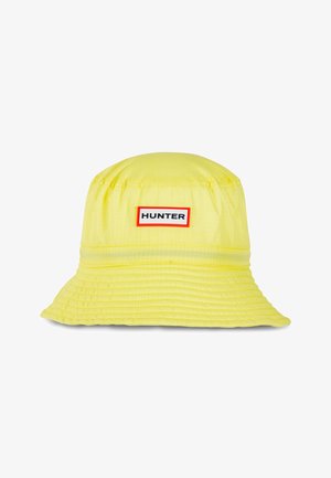 Sombrero tipo bucket amarillo con ala cosida y una etiqueta blanca rectangular con borde rojo que muestra "HUNTER" en letras negras.