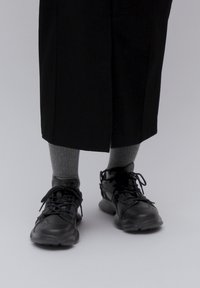 Black athletic shoes with textured soles, laces, and ventilation holes, paired with light gray knee-high socks, worn with black wide-leg pants.