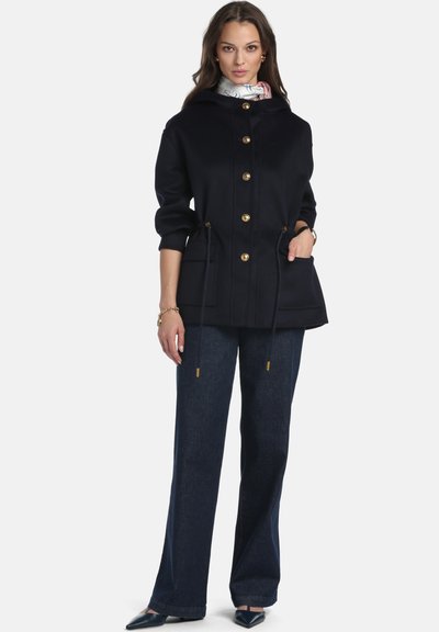 Cappotto in misto lana blu navy con cappuccio, bottoni dorati, vita con coulisse, tasche frontali, abbinato a pantaloni in denim scuro e scarpe con punta affilata.