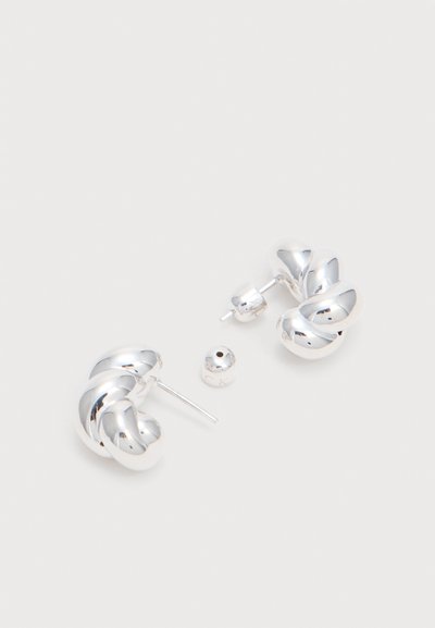 Boucles d'oreilles créoles épaisses en argent torsadé avec attaches amovibles sur une surface blanche unie.