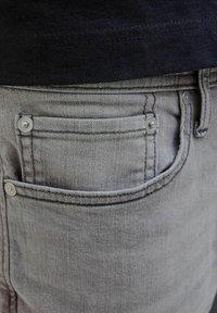 Grå denimjeans med silverfärgad hårdvara på bakfickan, med stickade sömmar och en texturerad finish.