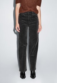 Zwarte corduroy wijde broek met een gestructureerd oppervlak en verticale ribbels, met een hoge taille en een knoopsluiting aan de voorkant, gecombineerd met zwarte enkellaarsjes.