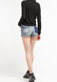 Černý top s dlouhým rukávem spárovaný se šortkami z denimové látky s světlomodrými a tmavomodrými záplatami, s ohrnutým lemem a černou obuví.