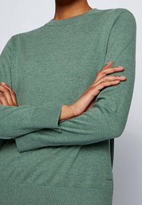 Grön stickad tröja med rund halsringning, ribbade mudd och strukturerad yta. Logodetalj vid f ållen. Mjuk och bekväm tyg.