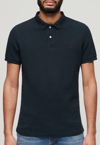 Donkerblauwe polo shirt van katoen met een gestructureerde afwerking, knoopsluiting met twee knopen en een subtiel geborduurd logo op de borst. Korte mouwen.