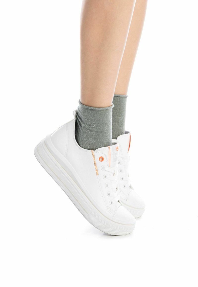 Zapatillas de lona blancas con suela de goma, con detalles en naranja y cordones visibles, combinadas con calcetines grises hasta el tobillo.