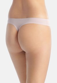 Lichtroze naadloze string, met een minimalistisch ontwerp, een soepele textuur en een lage taille. De achterkant toont een minimale bedekking.