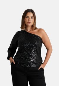 Top nero a spalla unica con paillettes su tutta la superficie, tessuto texturizzato e manica lunga su un lato, abbinato a pantaloni neri.