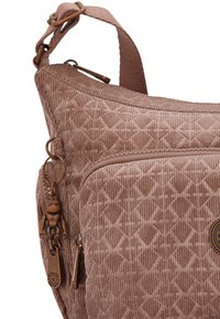 Braune Kordtasche mit Rautenmuster, einem Reißverschlussfach und bronzenen Hardware-Akzenten, ausgestattet mit einem dekorativen Anhänger am Reißverschluss.