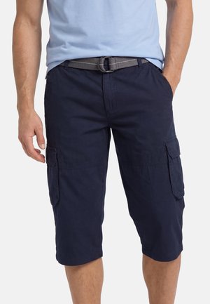 Mann trägt marineblaue Cargo-Shorts mit mehreren Taschen und einem grauen Gürtel, kombiniert mit einem hellblauen T-Shirt, Hände ruhen an den Seiten.
