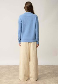 Jasnoniebieski sweter dzianinowy z kołnierzem szalowym, w zestawieniu z beżowymi spodniami typu wide-leg o prążkowanej teksturze. Miękka tkanina, luźny krój i długość pełna.