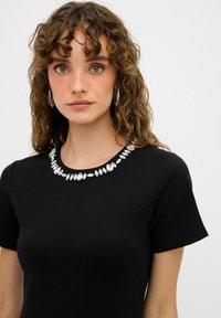 Schwarzes kurzärmeliges Kleid mit einem dekorativen Halsauschnitt aus Rhinestones und markanten, bohnenförmigen Akzenten, glatter Textur und figurbetonter Silhouette.