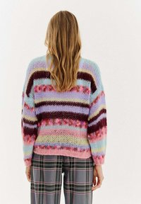 Sweter dzianinowy w pastelowych odcieniach z wielokolorowymi poziomymi paskami, charakteryzujący się luźnym krojem i miękkim, teksturowanym materiałem. Połączony z spodniami w kratę.