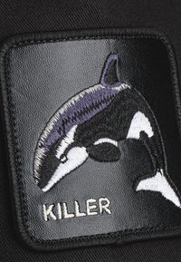Schwarzes Stoffpatch mit gesticktem Orca in Schwarz, Weiß und Lila, unter dem die Worte "KILLER" in weißen Stichen angebracht sind.