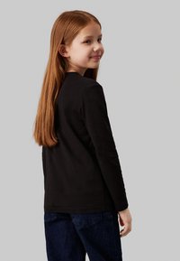 Camisa preta de manga longa feita de algodão, com decote redondo e um corte descontraído, combinada com jeans escuros. Costuras visíveis em destaque.