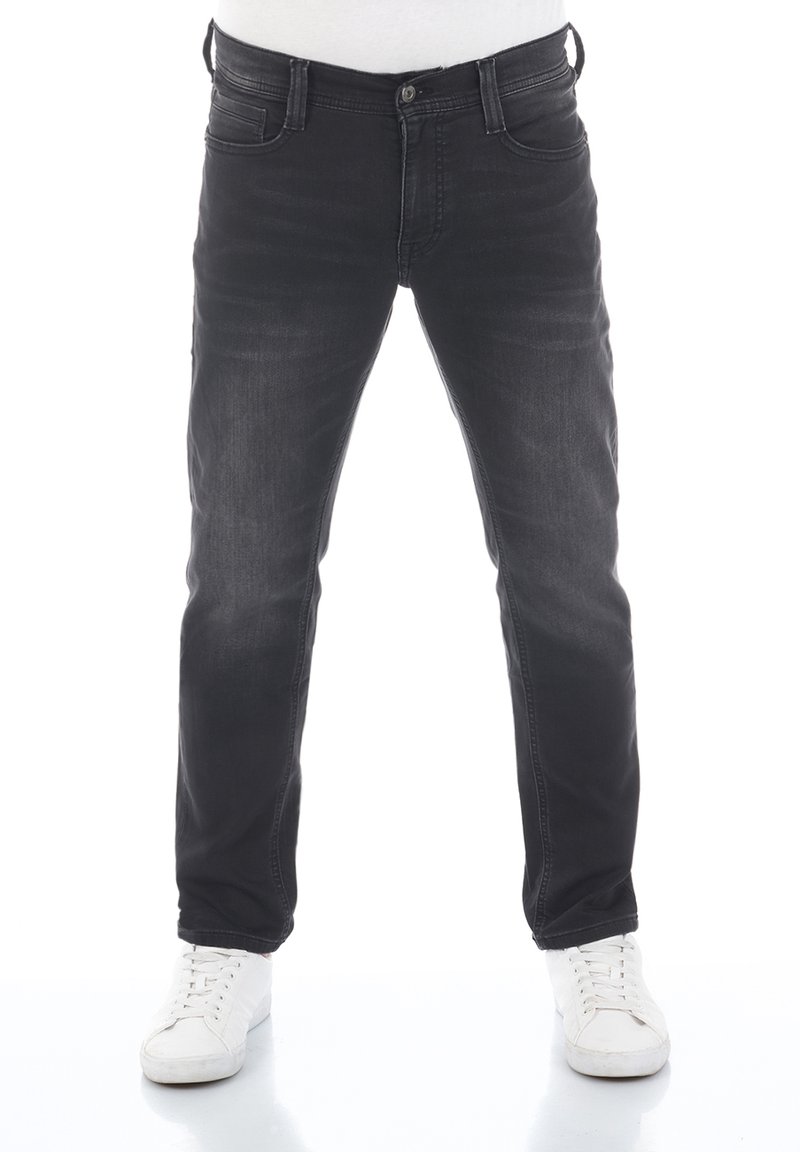 Jeans de mezclilla negra con un diseño ajustado, que cuentan con un estilo clásico de cinco bolsillos, un ligero desvanecimiento y un cierre de botón. Llevados con zapatillas blancas.