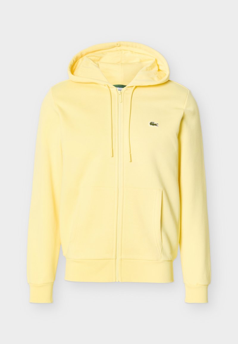 Sweat à capuche zippé jaune clair avec poches avant, cordon à la capuche et petit logo crocodile vert sur la poitrine gauche.