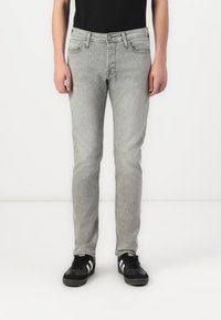 Lys grå denimjeans med slim fit, fem lommer og en falmet finish. Brukt med svarte joggesko med hvite striper.