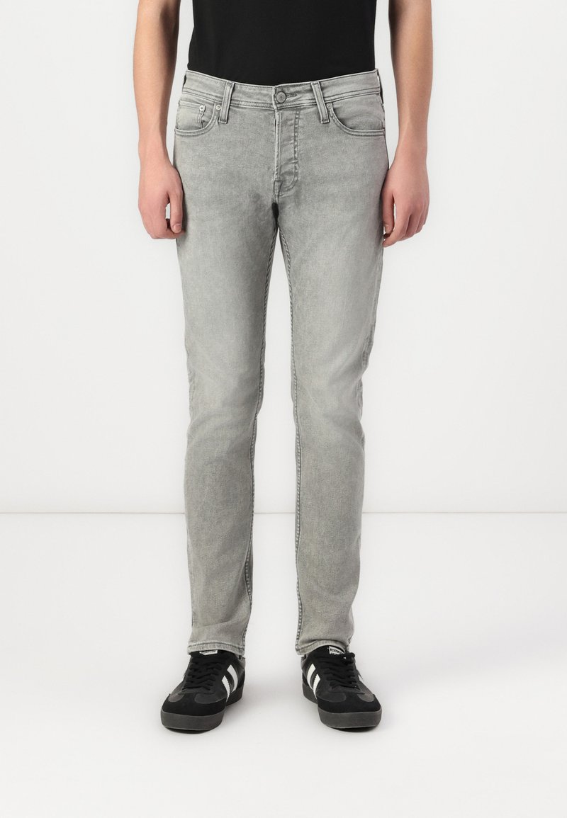 Lys grå denimjeans med slim fit, fem lommer og en falmet finish. Brukt med svarte joggesko med hvite striper.