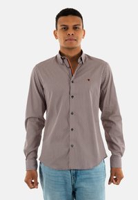 Chemise à manches longues en tissu à motifs avec des motifs de diamants rouges et bleus, un col boutonné et un contraste orange à l'intérieur du col.