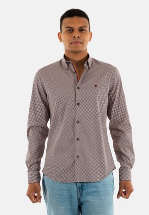 Chemise à manches longues en tissu à motifs avec des motifs de diamants rouges et bleus, un col boutonné et un contraste orange à l'intérieur du col.