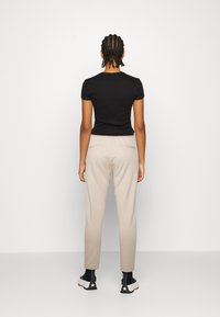 Zwarte getailleerde shirt met korte mouwen gecombineerd met beige elastische broeken. Gestructureerde zwarte enkellaarsjes met witte zolen. Eenvoudig, neutraal kleurenpalet.