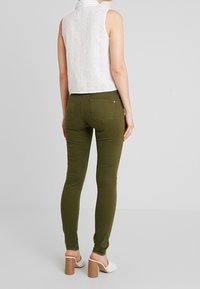 Bílá bezrukávová blůza s krajkovým vzorem, doplněná olivově zelenými slim-fit kalhotami. Bílé lodičky na podpatku s texturovaným vzorem dotvářejí tento outfit.