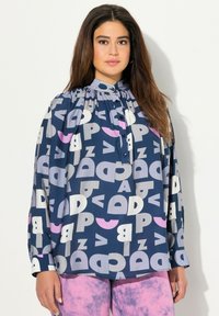 Blusa blu con motivo, caratterizzata da un colletto, maniche lunghe e un collo arricciato. I colori includono bianco, grigio e rosa in forme astratte e lettere.