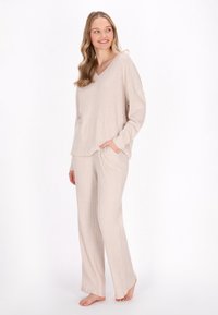 Beige, ribattu loungewear-setti, jossa on V-pääntie, pitkät hihat ja sivutaskut rentoa istuvuutta varten. Pehmeä rakenne suoraan leikatut housut.